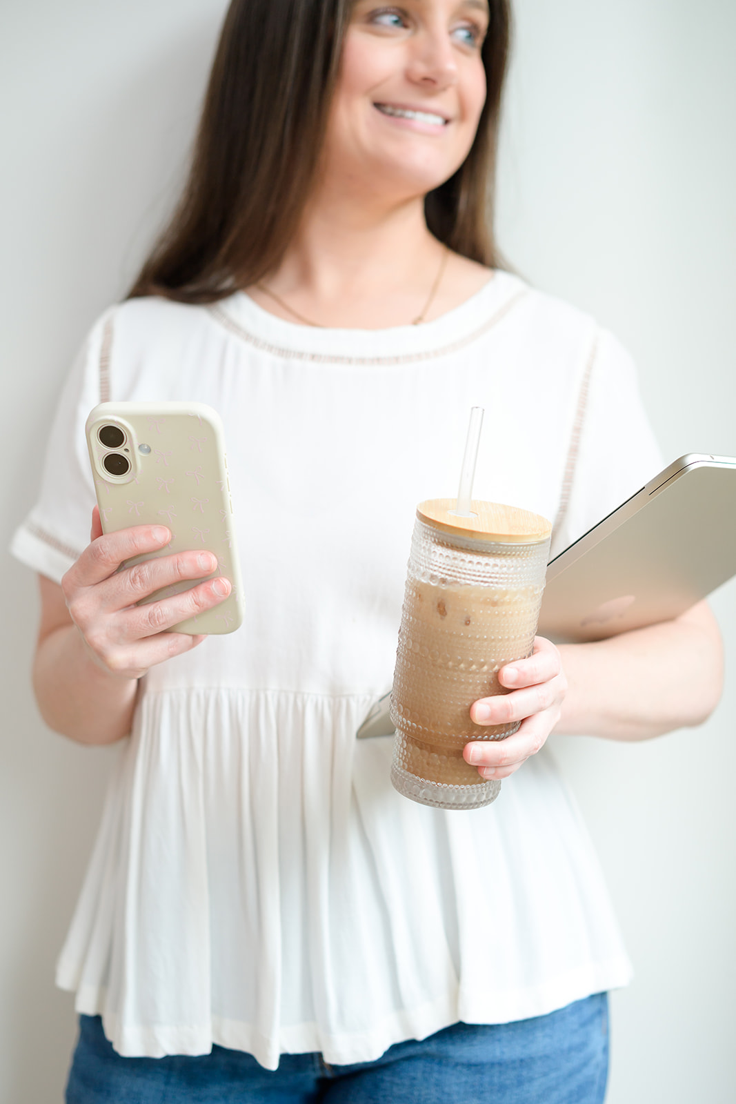 Chelsea holding her phone, an iced coffee and a laptop
