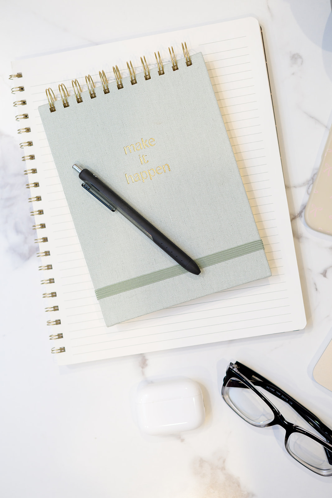 Sage notebook embossed with make it happen, with a pen and glasses